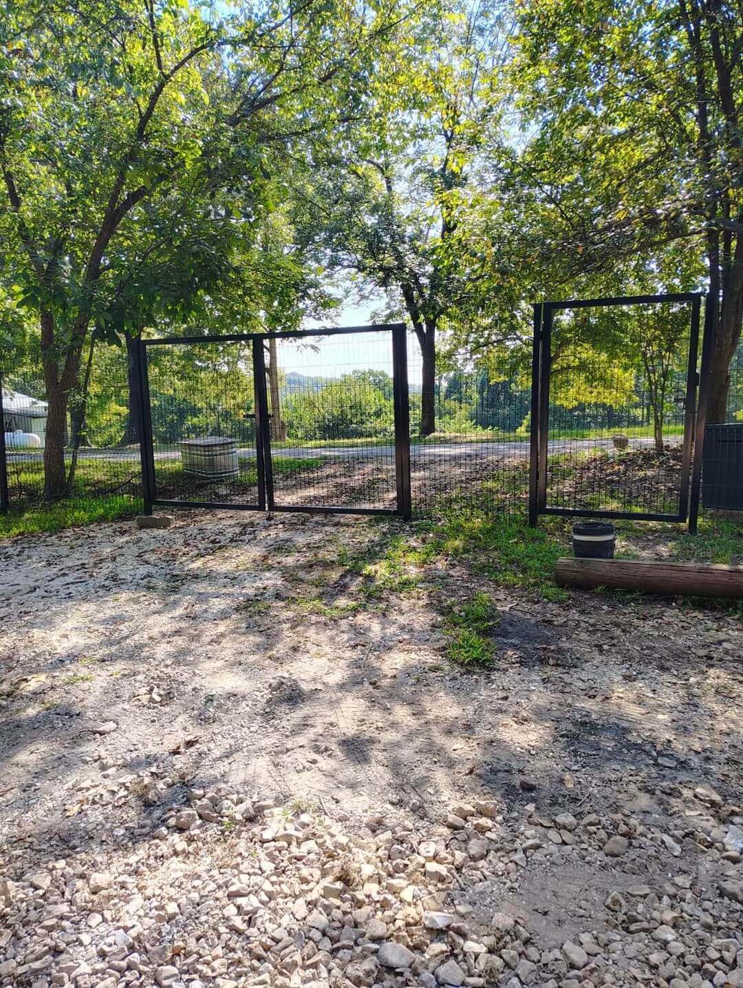 Black 3D welded wire fence with open gate running along a wooded driveway