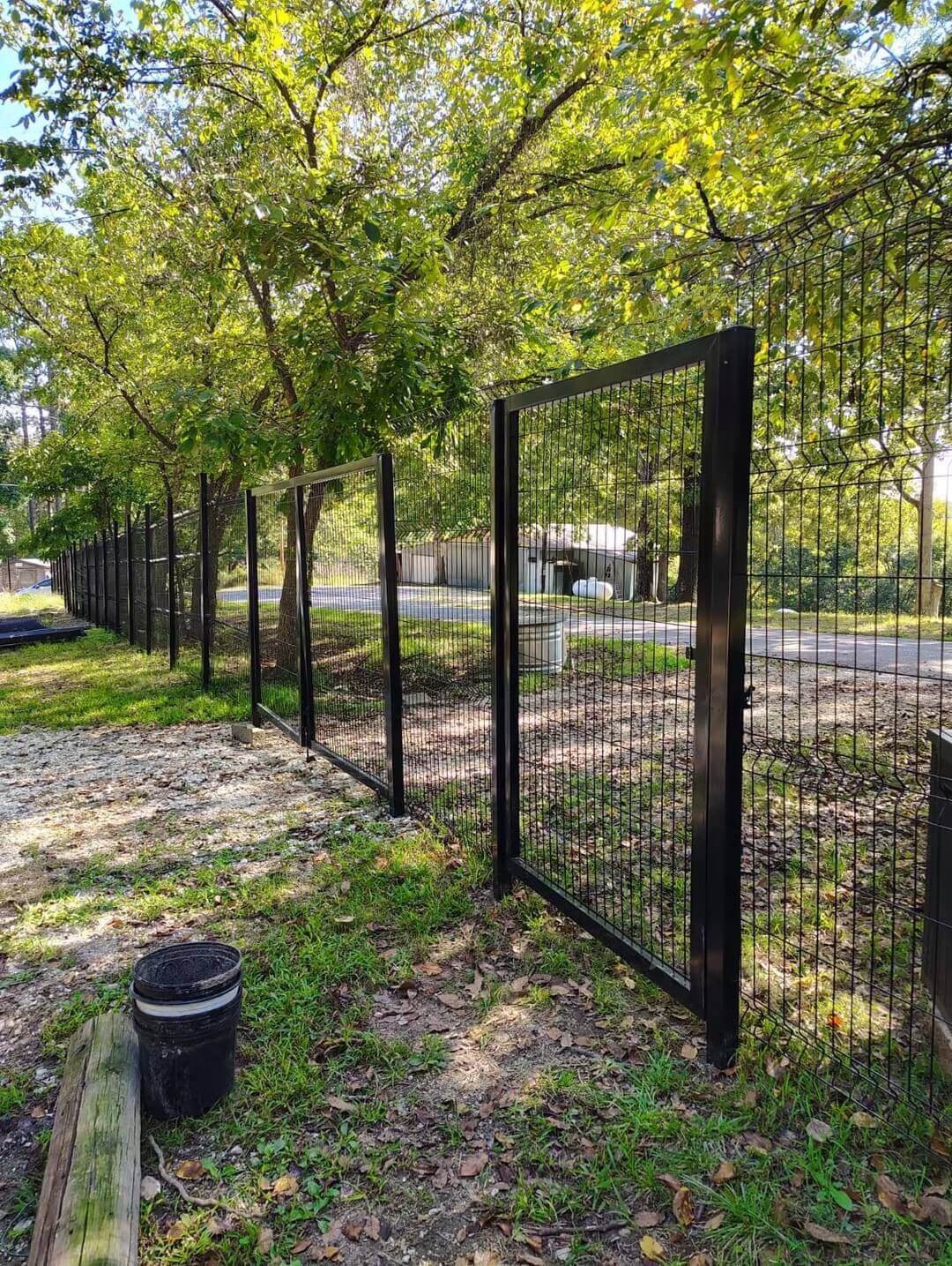 Matte black double-leaf drive gate at a wooded property entrance